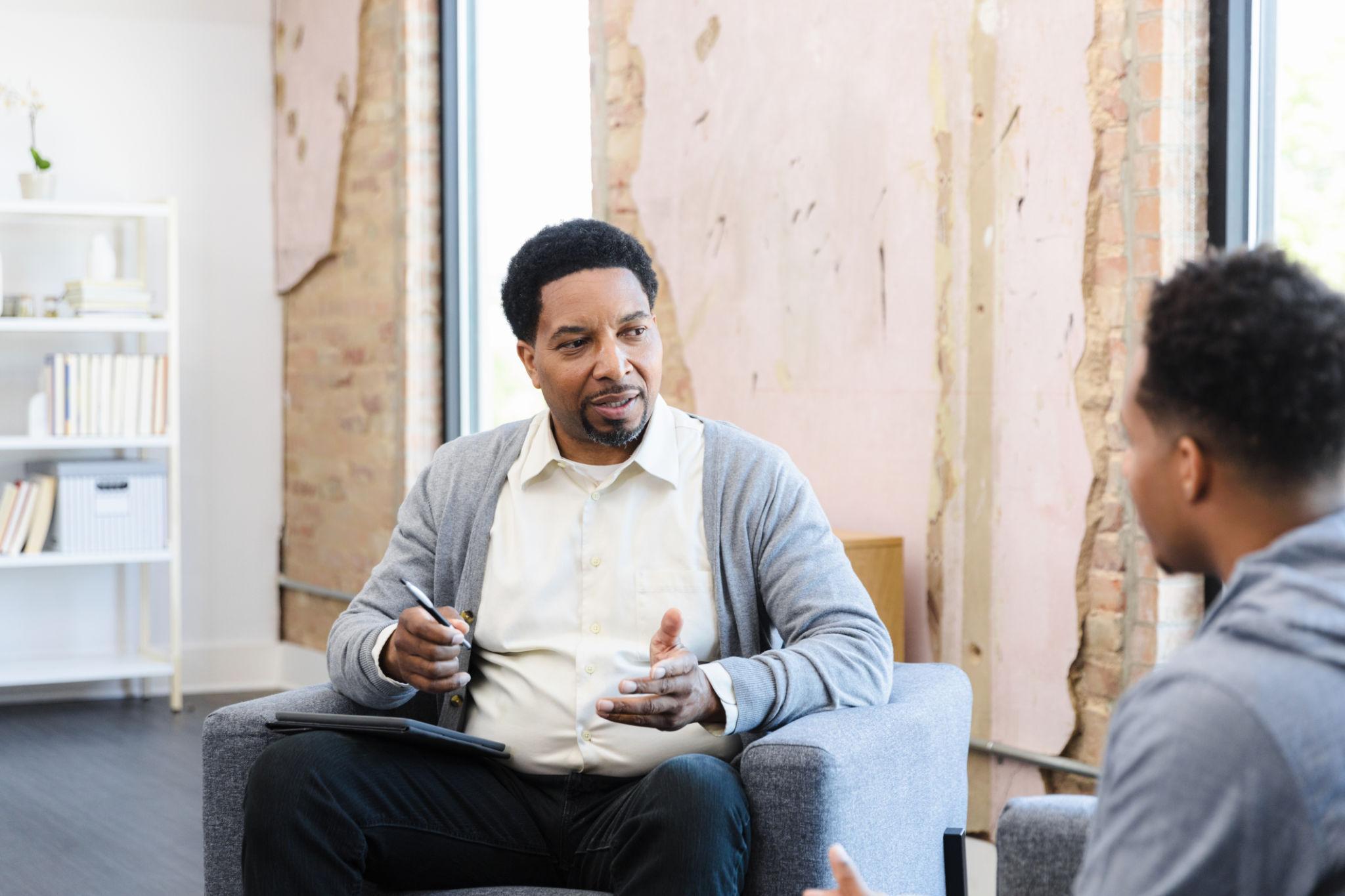 Black male mental health therapist speaking with a client during a counseling session.